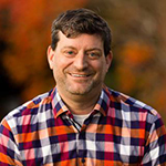 Jeff Witzel wearing a blue, red, white plaid shirt and smiling