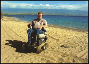 A man using a power wheelchair on the beach.