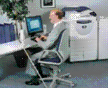 A man, who uses a white cane, sitting at a computer desk.